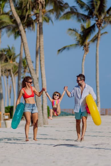 Eltern in Strandausrüstung heben ihr Kind in der Mitte hoch.