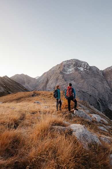 Zwei Wandernde mit Rucksäcken stehen auf einem schmalen Berggrat und blicken auf felsige Dolomitengipfel im warmen Licht