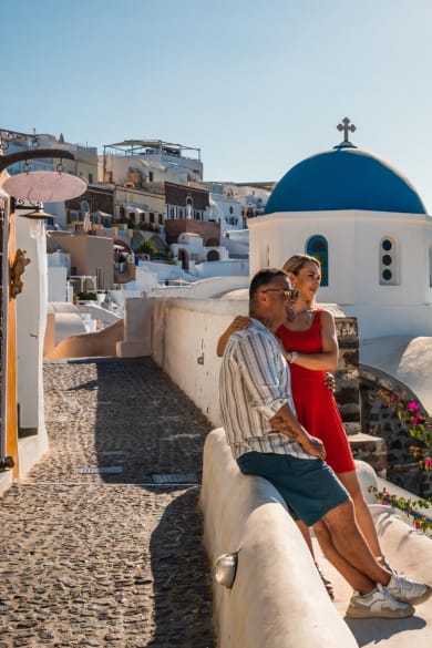 Ein junges Paar sitzt auf der Mauer auf Santorini und schaut aufs Meer.