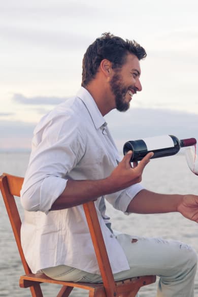Paar am Strand, Mann gießt Wein in ein Glas ein in Griechenland