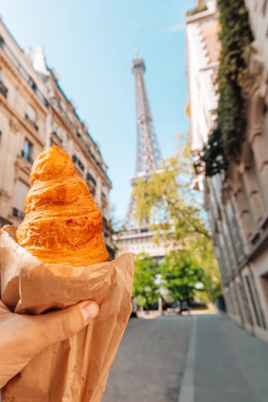Eine Person mit einem Croissant vor dem Eiffelturm in Paris, Frankreich © Alexander Spatari/Moment via Getty Images