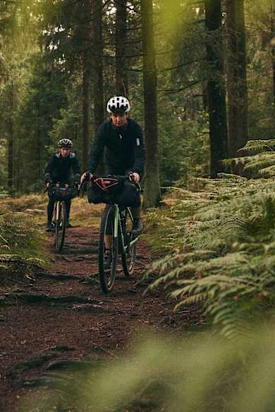Zwei Radfahrerinnen fahren durch einen dunklen Nadelwald