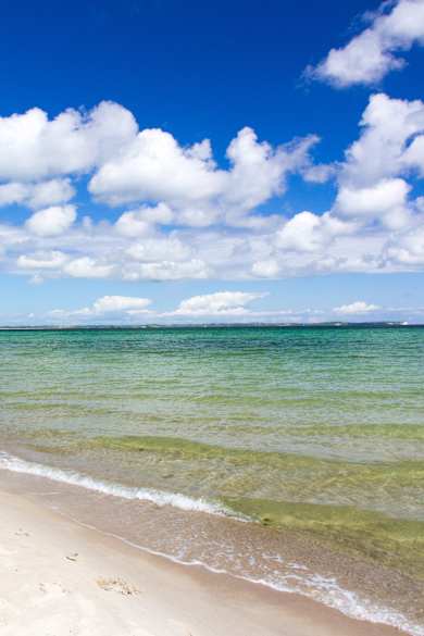 Ein langer leerer Strandabschnitt. In der Ferne spazieren zwei Menschen