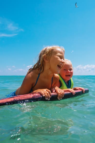 Zwei Kinder schwimmen mit einem Schwimmbrett im Meer.