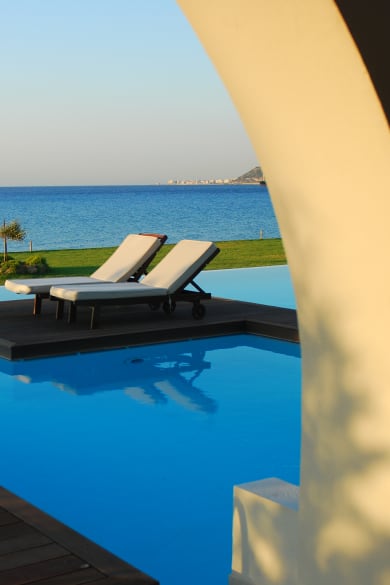 Zwei Sonnenliegen an einem Pool mit Meerblick auf Rhodos, Griechenland.
