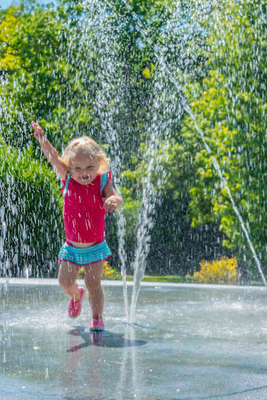 Kleines Mädchen läuft fröhlich durch einen Wasserbrunnen im Sommer.