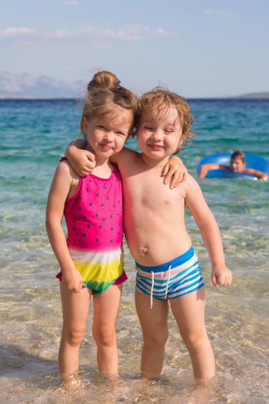 Zwei Kinder stehen Arm in Arm in kristallklarem Meer.