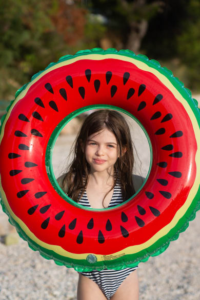 Mädchen hält einen Schwimmring in Melonen-Optik an einem Strand in Kroatien hoch.