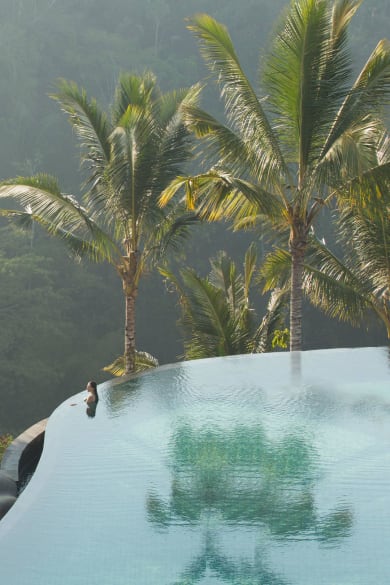 Frau in einem Infinity-Pool schaut auf den umliegenden Dschungel