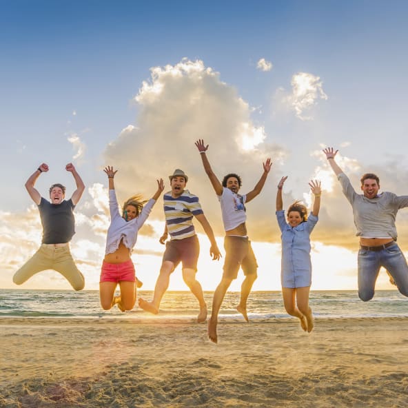 Eine Gruppe von FreundInnen springt an einem Strand in die Luft.