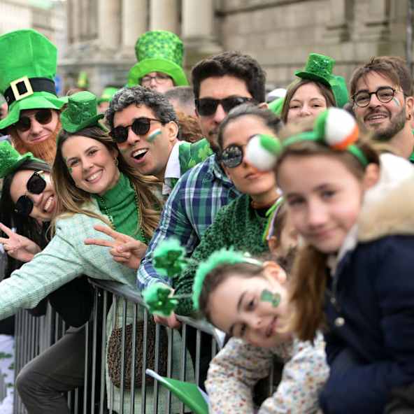Menschen stehen verkleidet hinter einer Absperrung bei der St. Patrick's Day Parade in Irland.