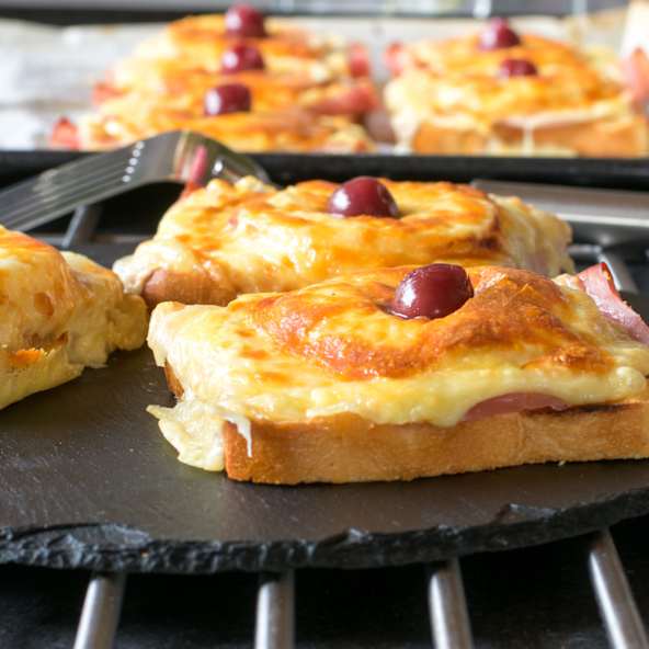 Überbackender Toast Hawaii mit Schinken, Käse und einer Kirsche.