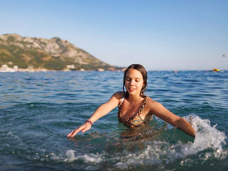Ein Mädchen im Teenageralter dreht sich im Kreis im Meer © iStock.com/YouraPechkin