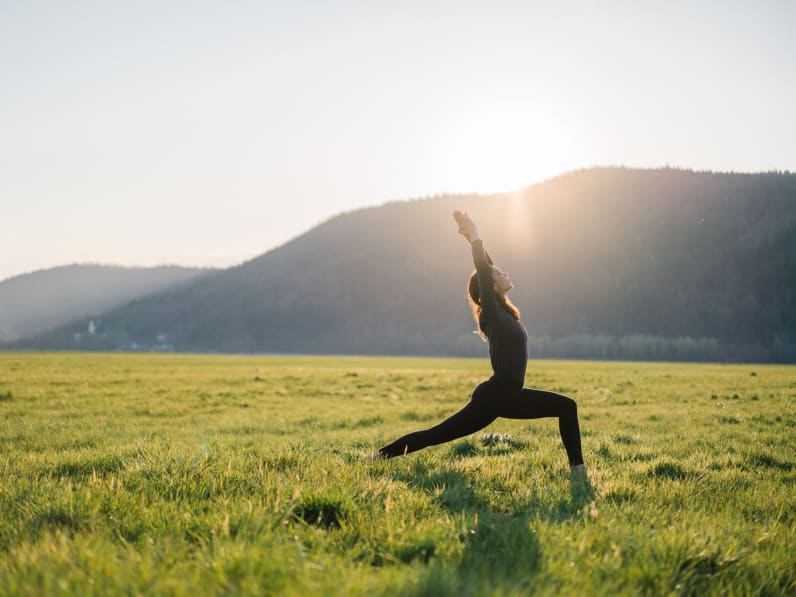Junge Frau übt Yoga in grasbewachsener Wiese bei Sonnenaufgang © iStock.com/AscentXmedia