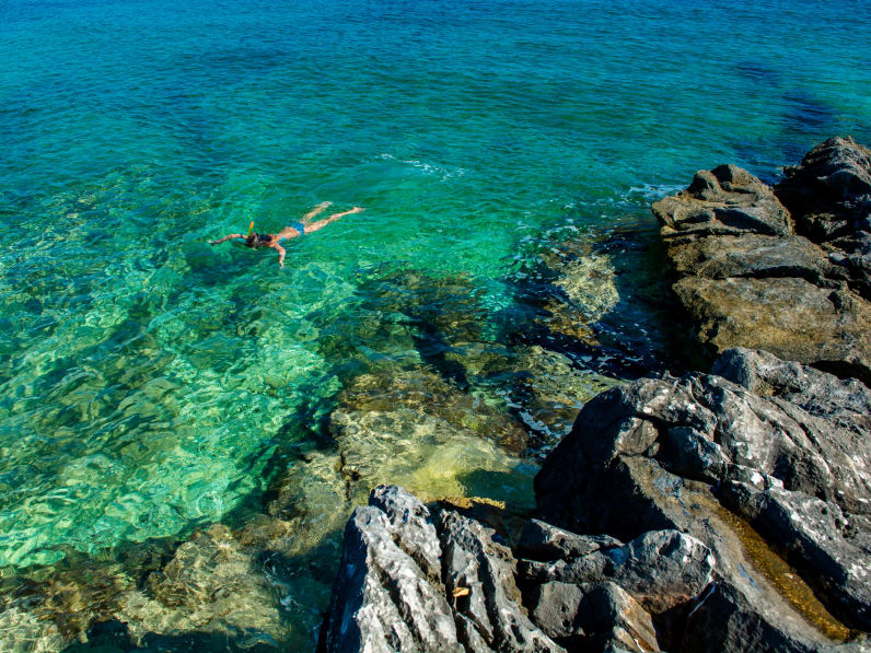 Junges Mädchen schnorchelt durch türkisfarbenes Wasser an der Küste © iStock.com/grafxart8888