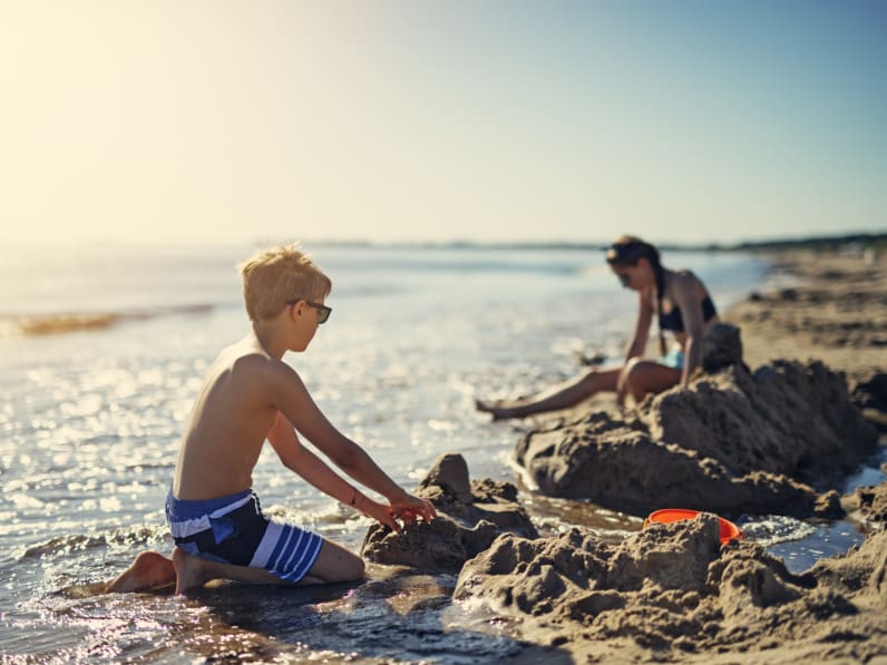 Kinder spielen am Strand und bauen eine Sandburg © iStock.com/Imgorthand