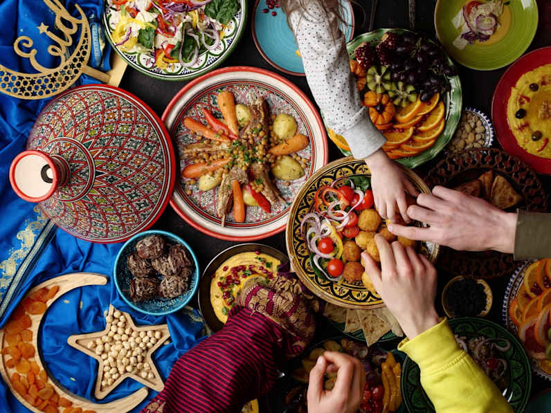 Blick von oben auf eine Vielzahl von Gerichten, mehrere Hände greifen nach Essen