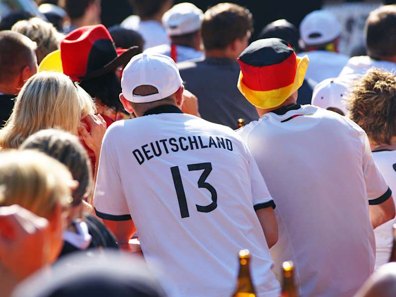 Fans in Deutschlandtrikots sitzen draußen beim Public Viewing