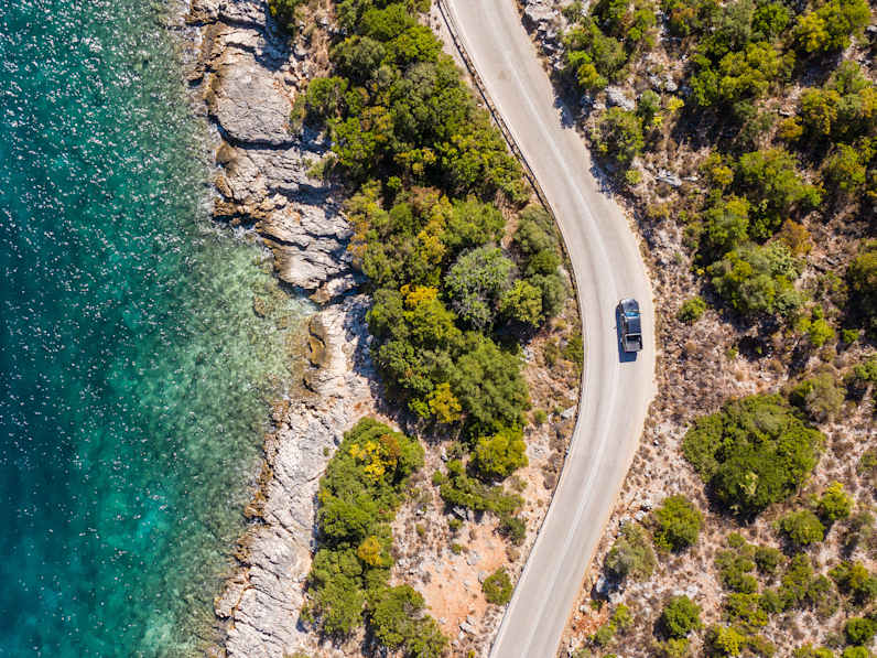 Blick von oben auf ein Auto auf einer Straße am Meer