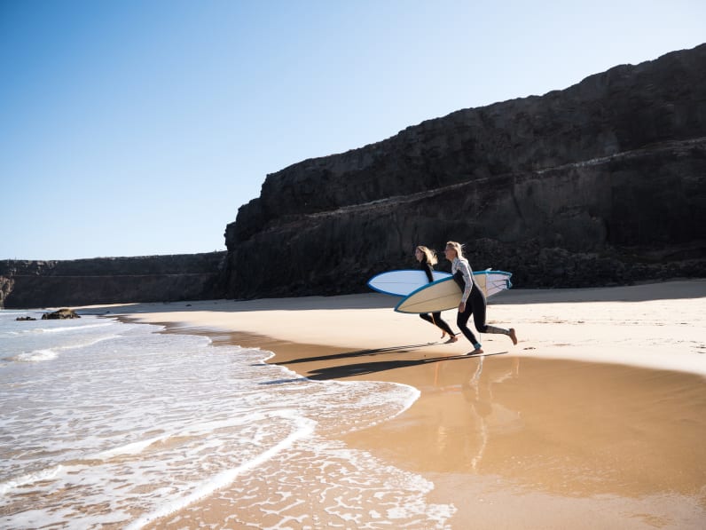 Surferinnen am Strandufer rennen zu den Wellen © iStock.com/1MEDIA