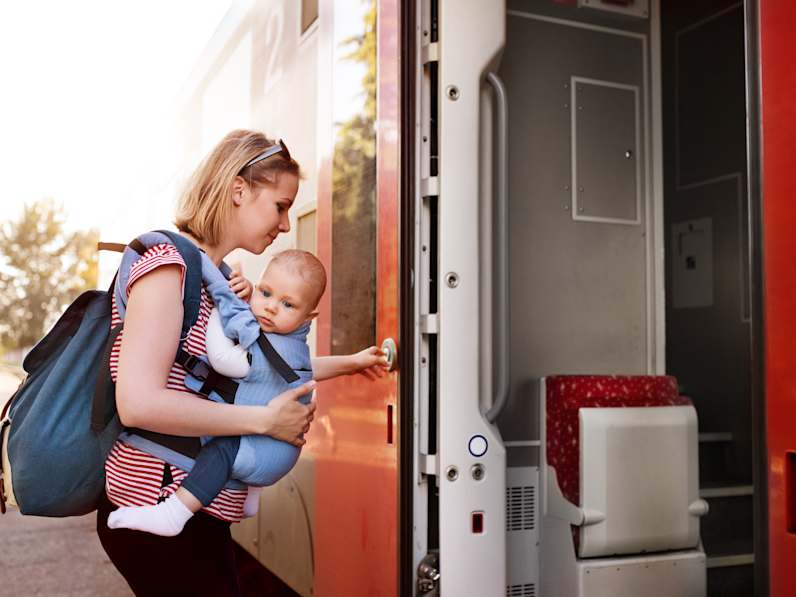 Frau mit Baby in der Trage steigt in einen Zug