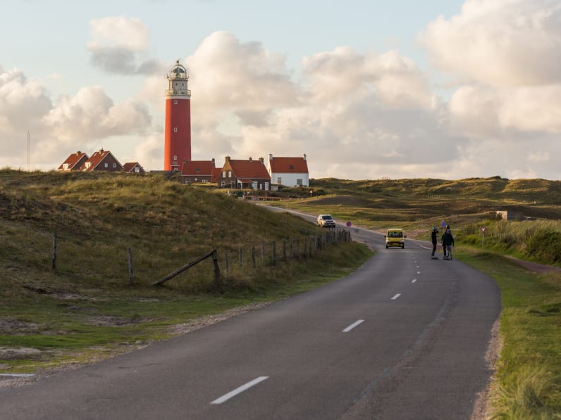 Autos und Fußgänger auf einer Straße zu einem Leuchtturm in Nordholland, Niederlande.