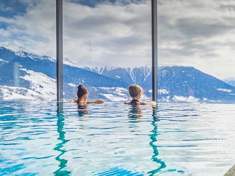 Zwei Frauen in einem Pool blicken auf eine bergige Landschaft