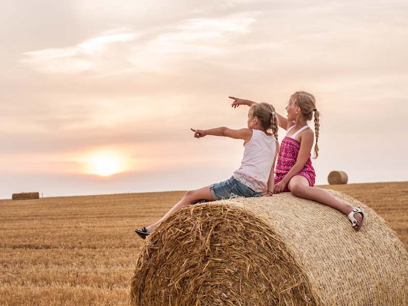 Zwei Mädchen sitzen auf einem Bauernhof.