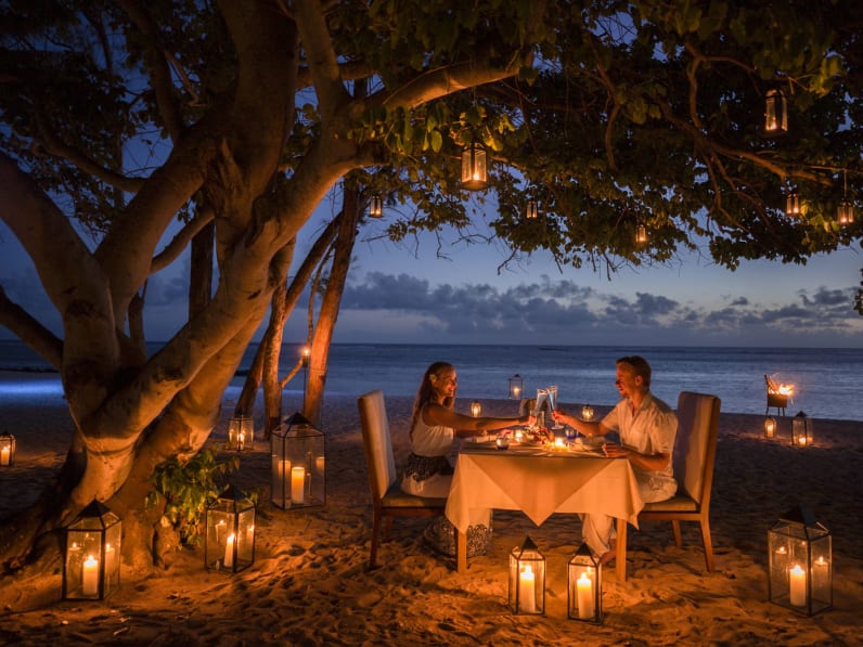 Am Strand von Mauritius, unter einem Baum, sitzt ein Paar, umgeben von Kerzen, an einem Tisch