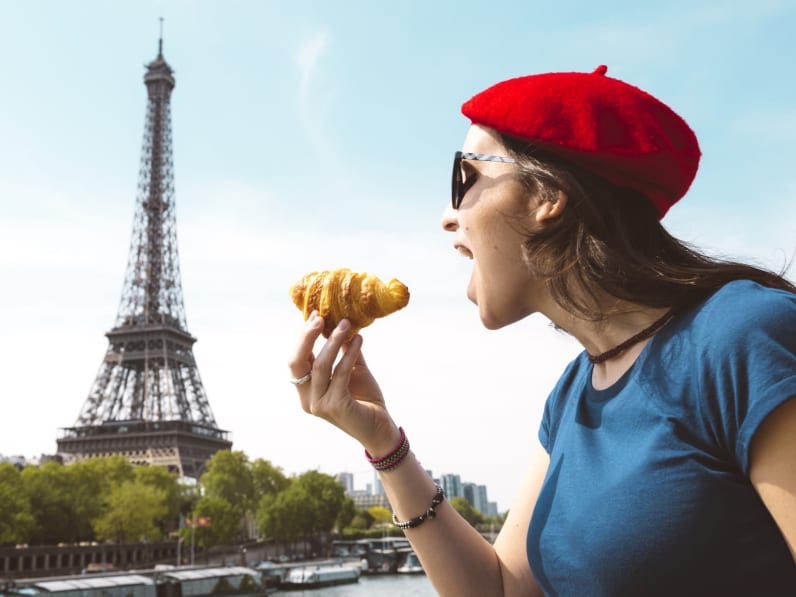 Eine Frau isst ein Croissant vor dem Eiffelturm.