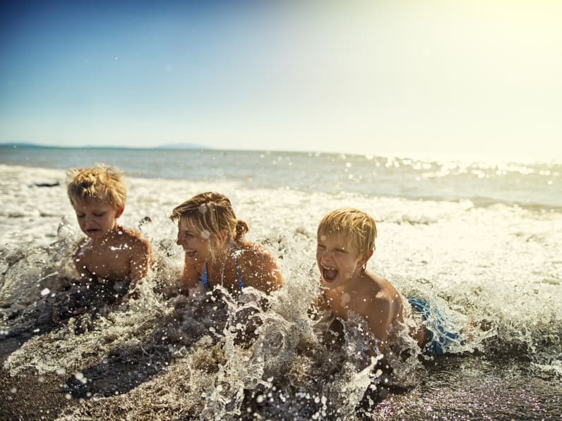 Familie liegt am Strand und planscht in Meereswellen in der Toskana, Italien