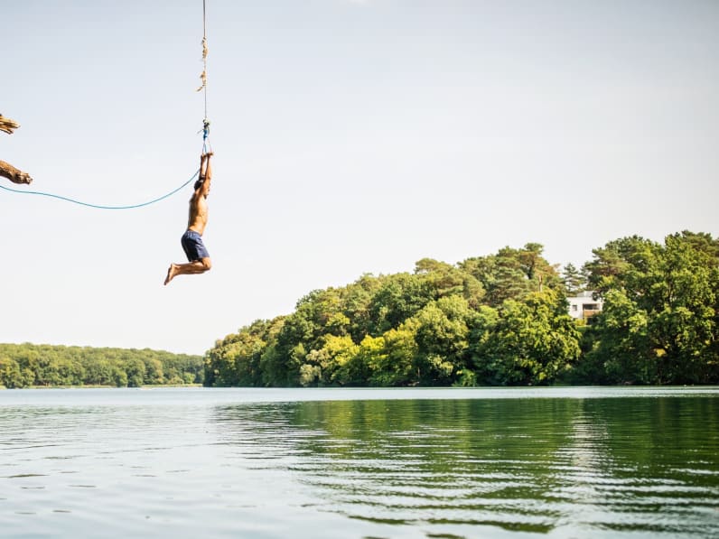 Ein Mann springt an einer Liane ins Wasser.