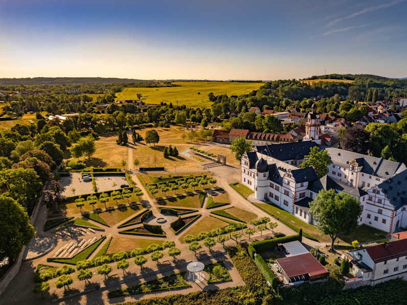 Luftperspektive auf ein Schloss am Rande einer Stadt, welches an einen großen, geometrischen Garten angrenzt.