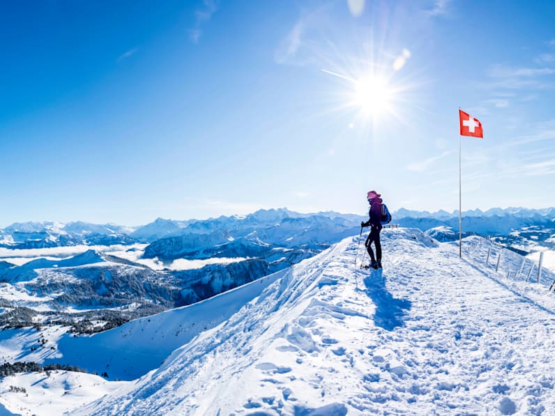 Ein Wanderer steht vor einer Schweizer Fahne auf einem Berg in den Alpen.