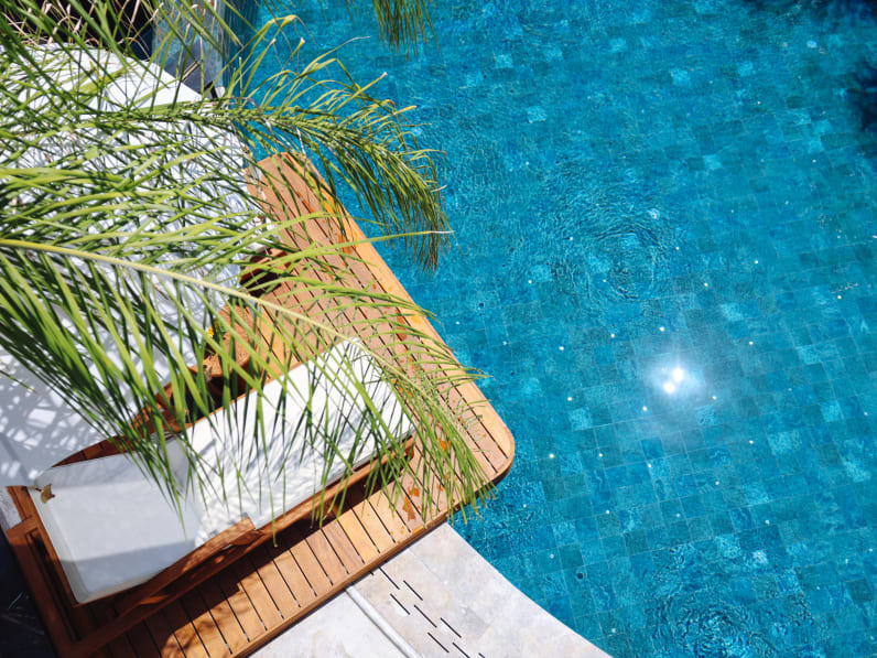Liegen unter Palmen am blauen Hotelpool.