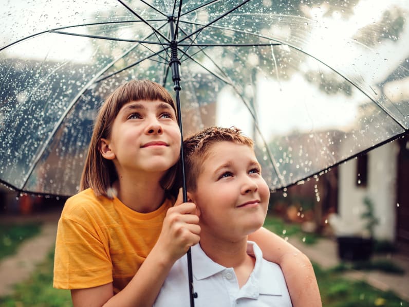 Zwei Kinder stehen gemeinsam unter einem Regenschirm. © Kerkez/iStock / Getty Images Plus via Getty Images