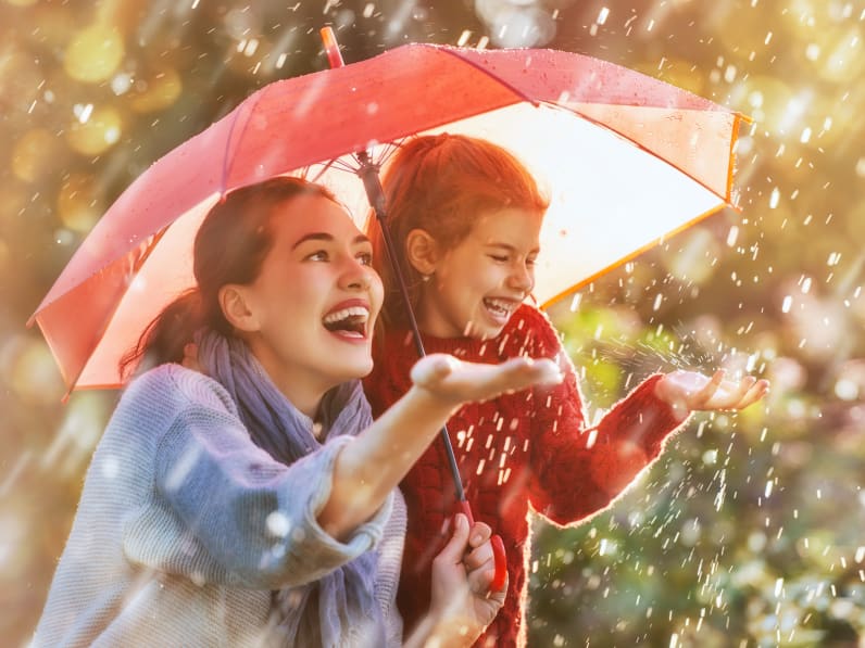 Mutter mit Kind bei Regen glücklich unter Regenschirm.