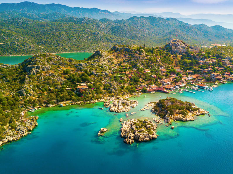 Blick auf die Weite der Türkischen Riviera mit grüner Landschaft. Im Vordergrund ist das blaue Meer zu sehen.