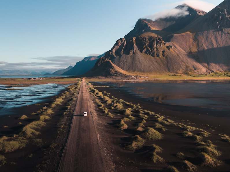 Ein Auto fährt bei Sonnenaufgang auf einer Küstenstraße in Island. (c) 2025 SamPronk1/Shutterstock.