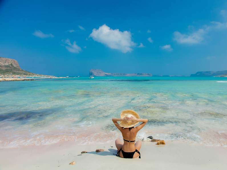 Mädchen im schwarzen Bikini und mit Hut am Strand von Balos © GettyImages