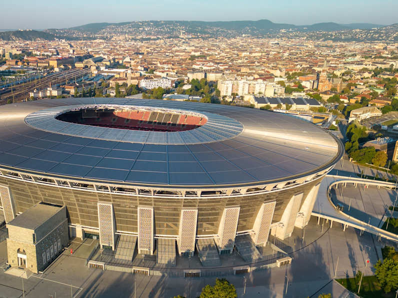 Luftaufnahme des Stadions der Puskas Arena in Budapest mit Skyline und Zuglinien im Hintergrund©Shutterstock | Wirestock Creators