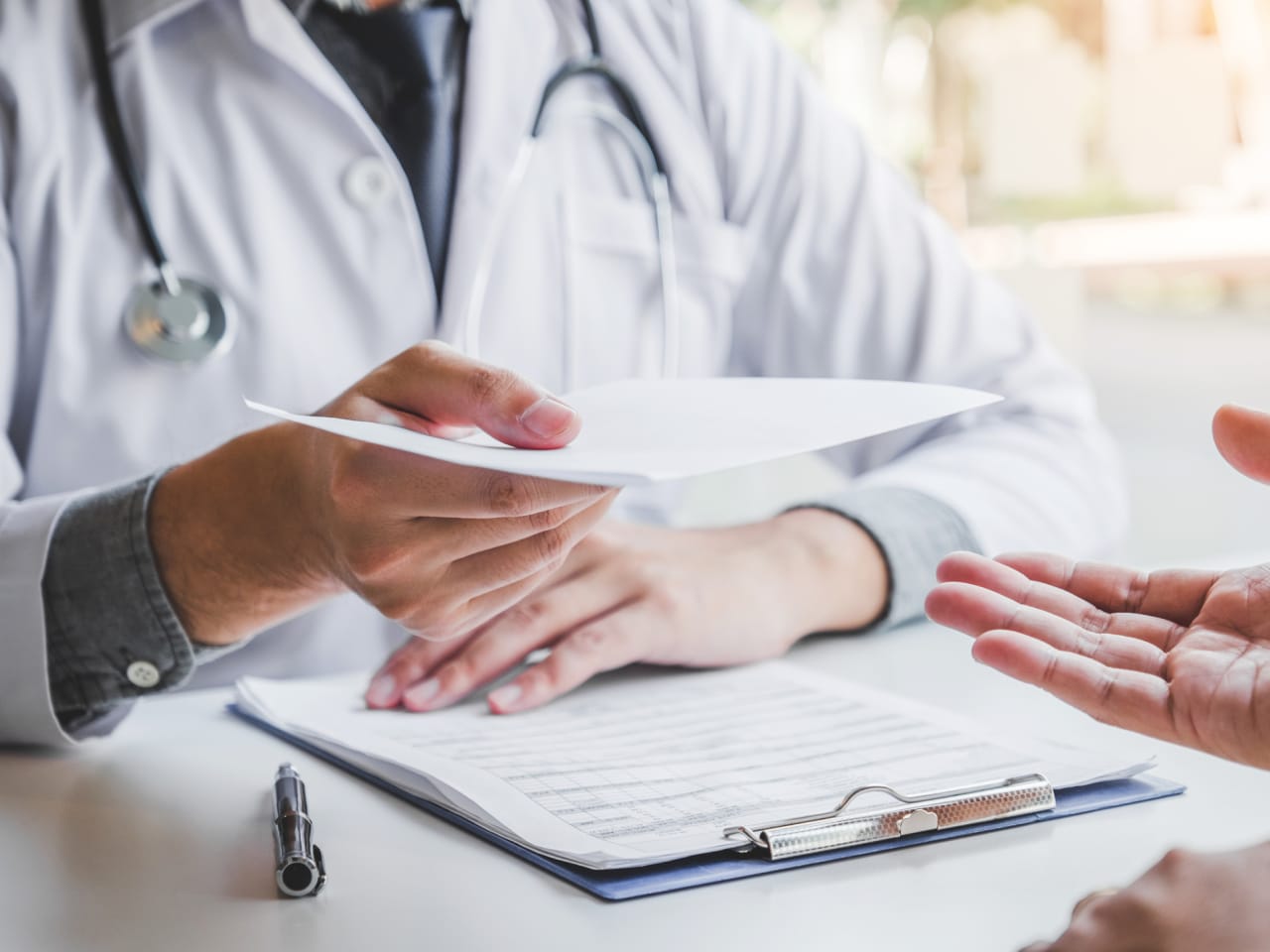 Arzt schreibt eine Diagnose und gibt ein ärztliches Rezept an einen Patienten ©iStock.com/SARINYAPINNGAM