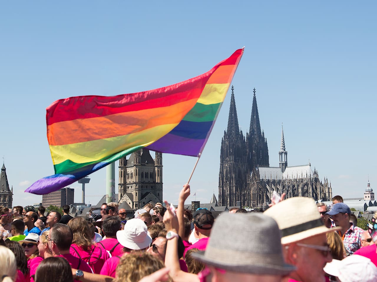 Menschenmenge mit großer Regenbogenflagge in der Nähe des Kölner Doms