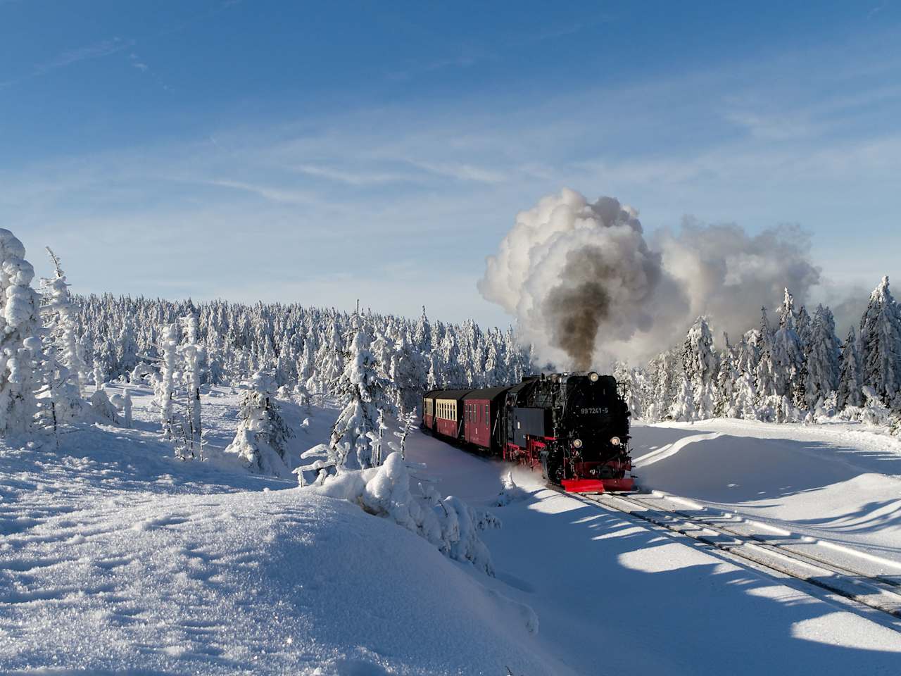 Eine schwarze Dampflok fährt durch eine tief verschneite Landschaft im Harz, umgeben von schneebedeckten Bäumen.