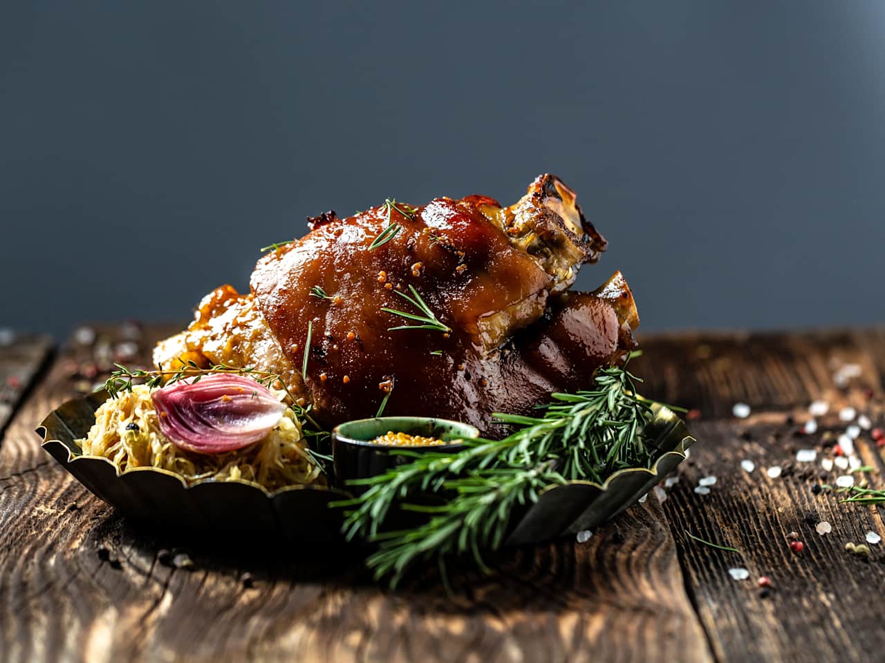 Zartes Eisbein mit Kraut und Senf in einer Schale mit Rosmarin auf einem rustikalen Tisch.