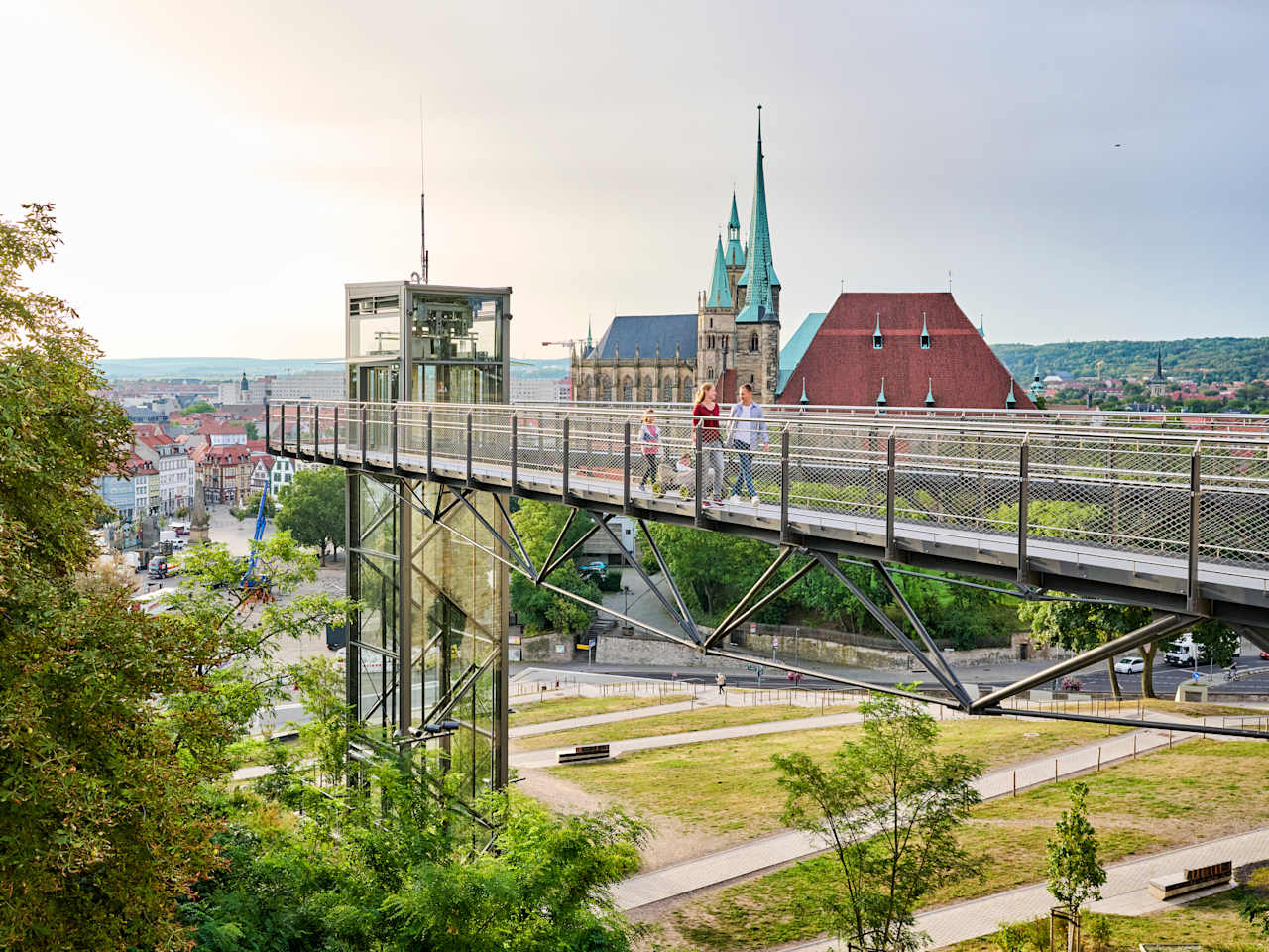 Ein Skywalk führt über einen Park, im Hintergrund liegt eine Kathedrale und eine Innenstadt mit historischen Fassaden