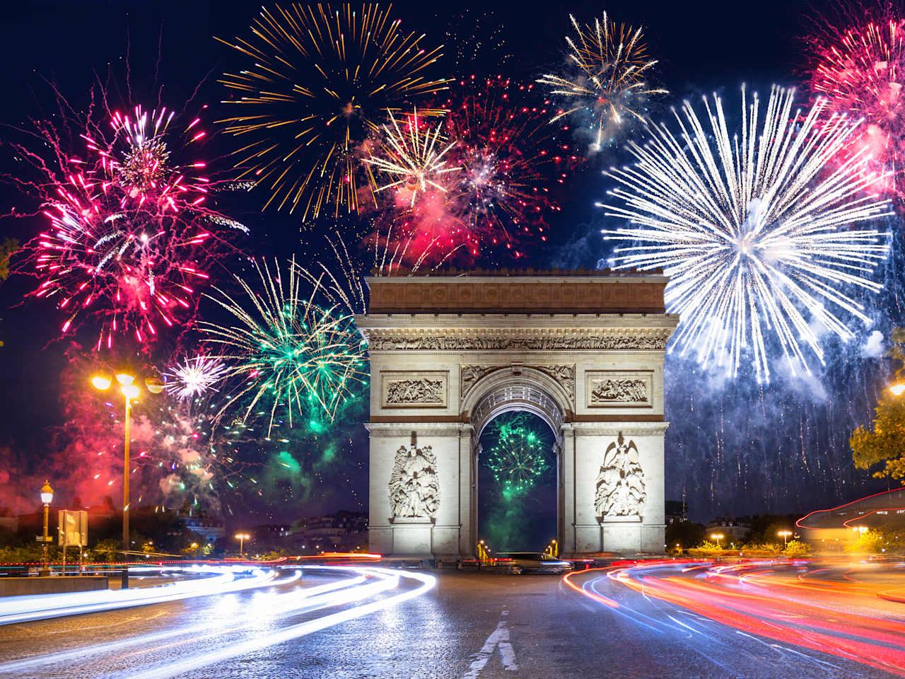 Der Arc de Triomphe in Paris vor einem dunklen Himmel voller Feuerwerk.