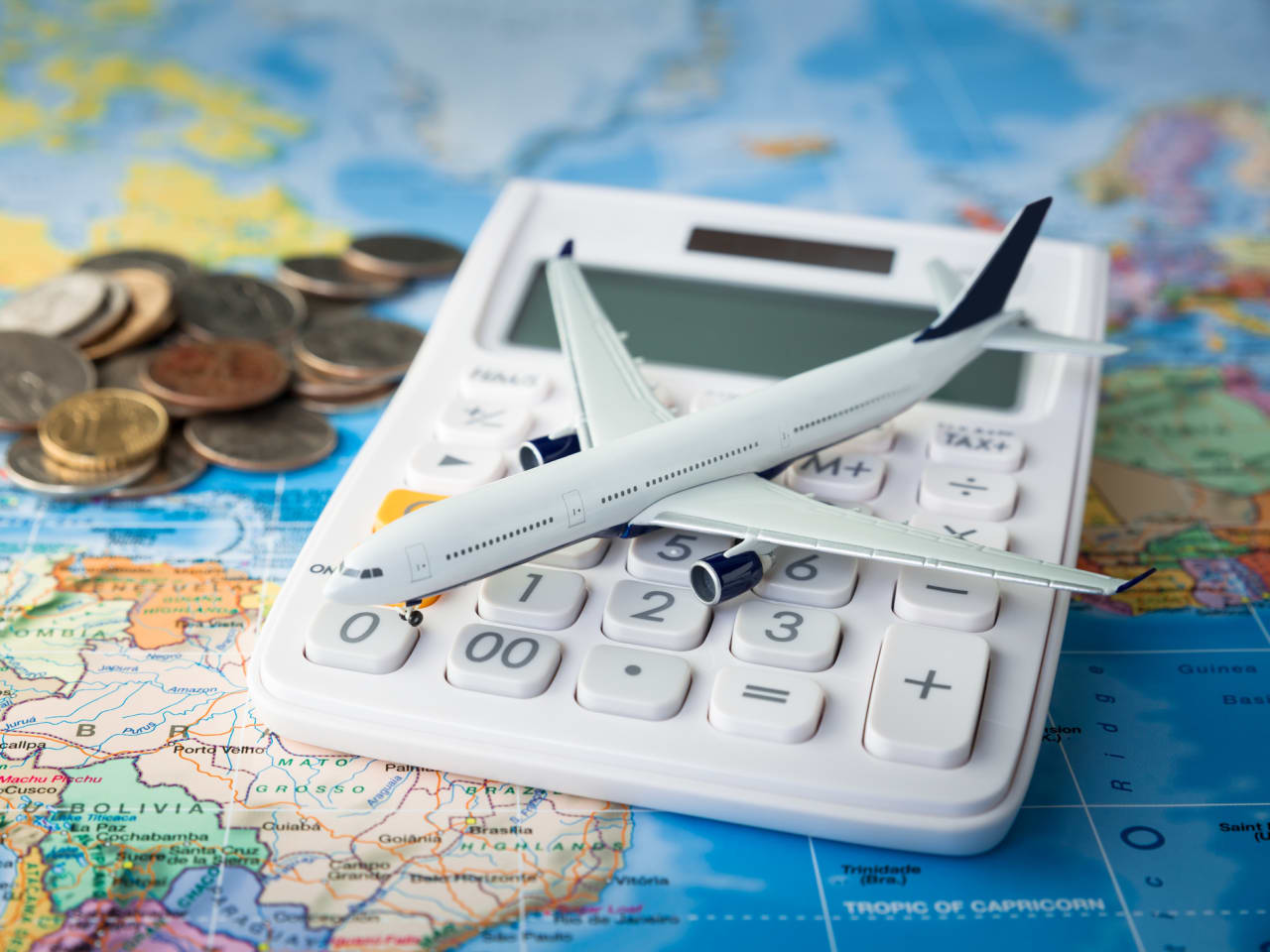 Flugzeug auf einem Taschnerechner mit Kleingeld auf einer Weltkarte © iStock.com/Sezeryadigar