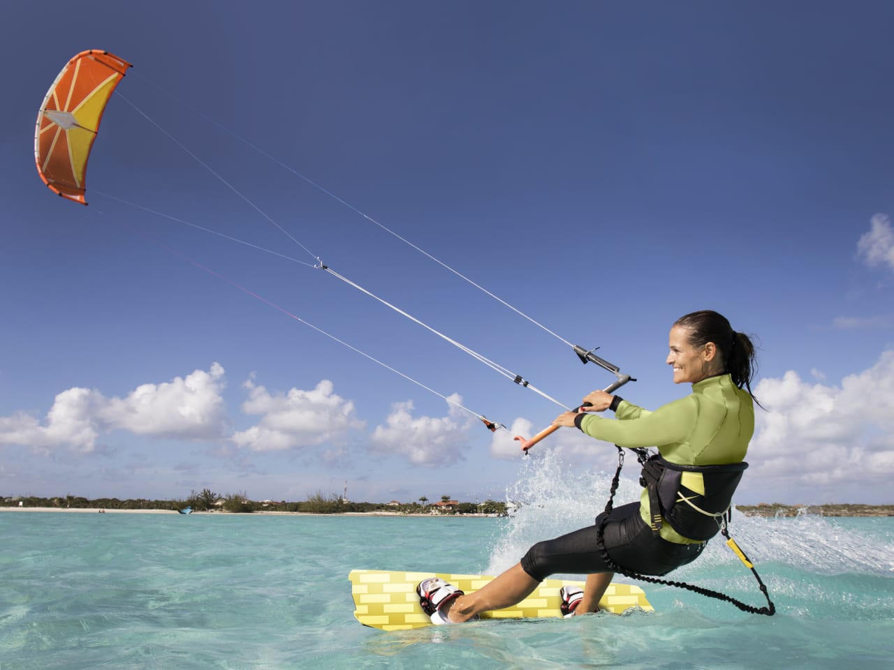 Frau hat Spass beim Kitesurfen in türkisfarbenem Meer © iStock.com/JMichl