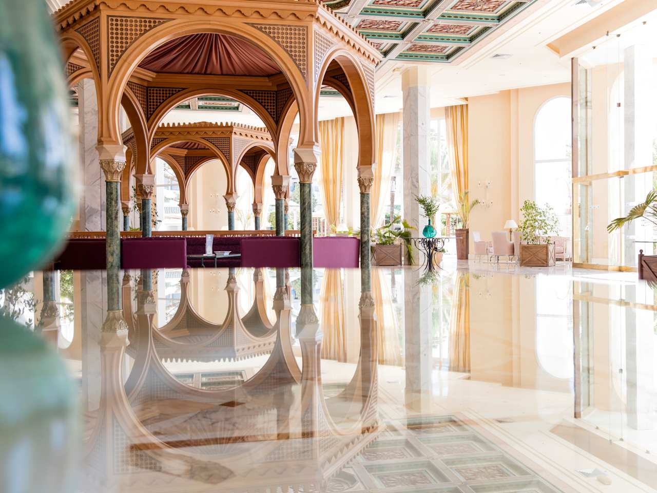 Das Bild zeigt ein modern eingerichtetes Wellnesszentrum. Der Blick geht über eine glatte Wasserfläche auf eine hölzerne Pagode. Die Fenster sind groß und an den Raumwänden stehen Blumen